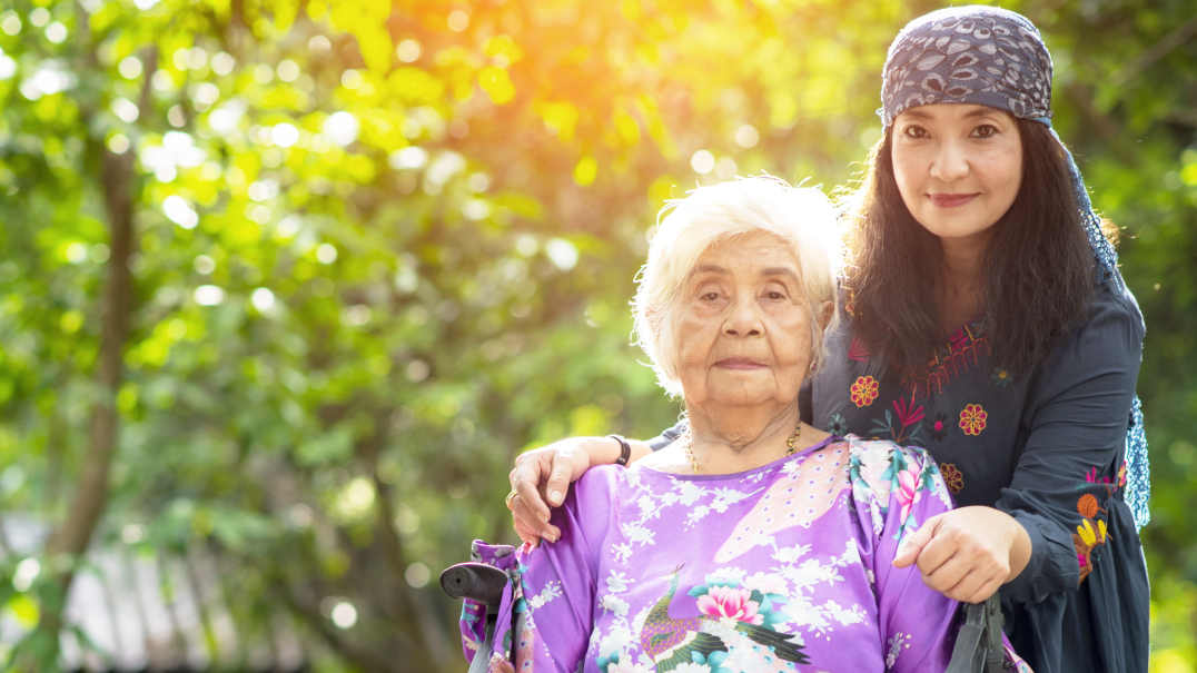 caregiving asian grandmother with granddaughter by wheelchair.png